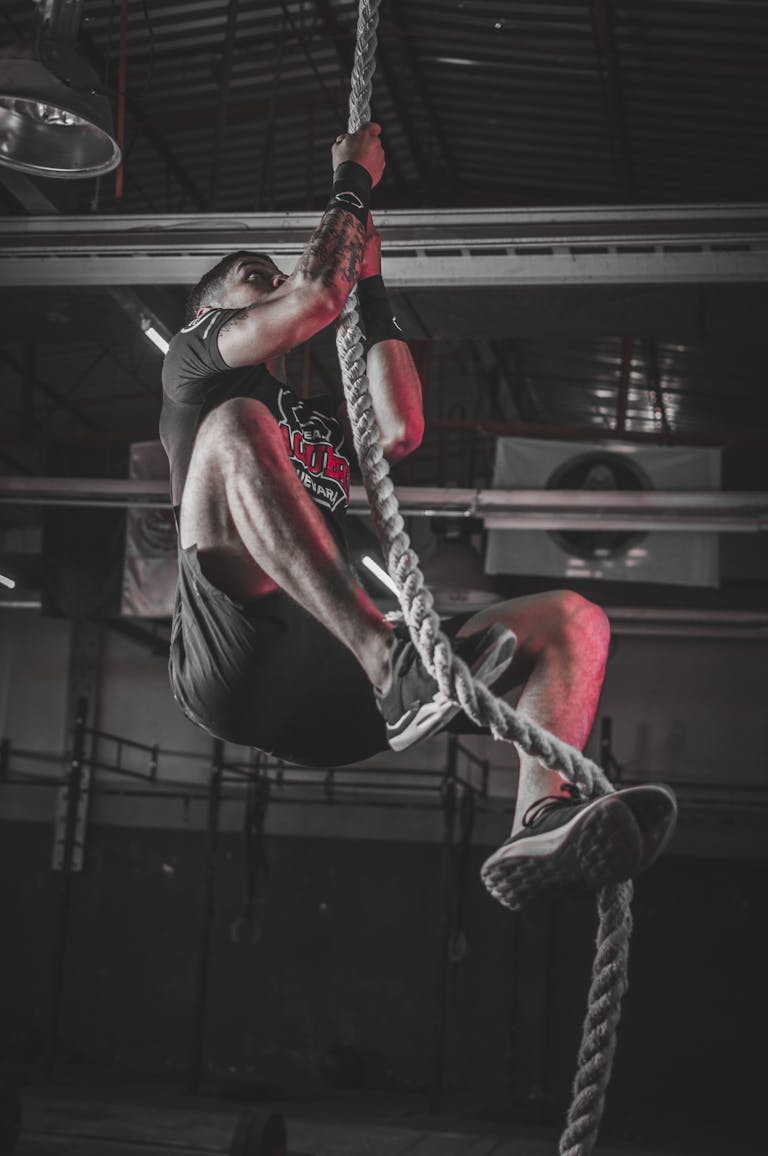 A determined man climbing a rope in an indoor gym setting, showcasing strength and fitness.