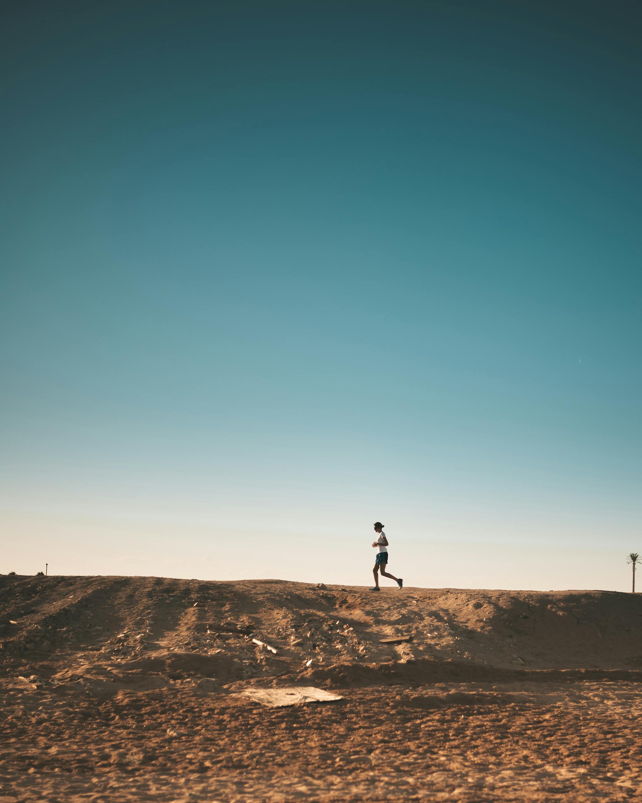 A person jogs on a sandy path with a vast blue sky above, capturing movement and freedom.